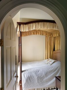 a canopy bed sitting in the middle of a bedroom next to a doorway with curtains on it