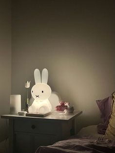 a white rabbit lamp sitting on top of a night stand next to a small bed