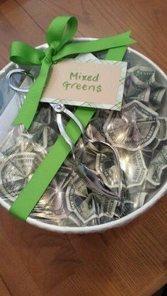 a bowl filled with lots of money sitting on top of a wooden table next to a green ribbon