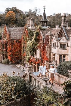 two people are walking down the street in front of some houses with ivy growing on them