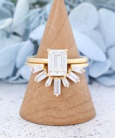 a gold ring with an emerald cut diamond in the center on top of a wooden cone