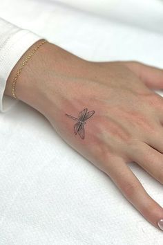 a woman's hand with a small dragonfly tattoo on it