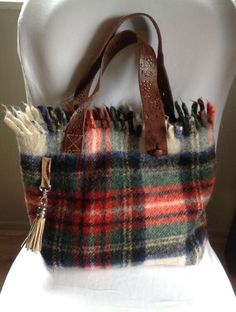 a plaid purse with tassels is sitting on top of a white cloth chair