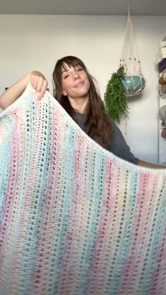 a woman is holding up a crocheted blanket