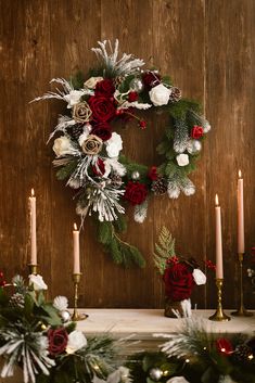 a wreath with red and white flowers sitting on top of a mantle next to candles