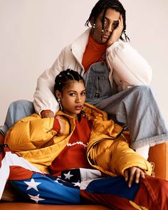 two people sitting on top of each other wearing jackets and pants with an american flag