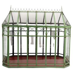 a green metal and glass greenhouse with red flooring on the side, isolated against a white background