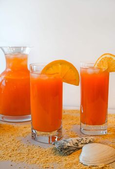 three glasses filled with orange juice and garnished with an orange slice on the side