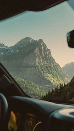 the view from inside a car looking at mountains and trees in the distance, with one person driving