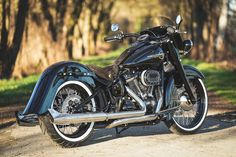 a black motorcycle parked on the side of a dirt road in front of some trees