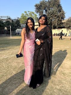 two women in sari standing next to each other on a field with people behind them