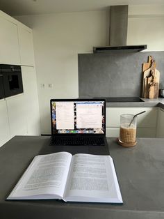 an open book sitting on top of a table next to a laptop computer and drink