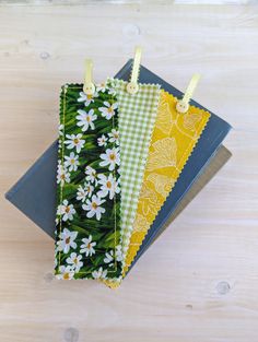 three notebooks are lined up on top of each other, one is yellow and the other has white daisies