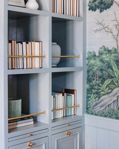 a book shelf filled with lots of books next to a wallpapered wall behind it