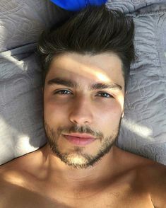 a shirtless man laying on top of a bed next to a blue feather hat