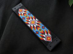 a colorful beaded wristband on a black shirt with green leaves in the background