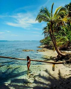 a woman standing on top of a sandy beach next to the ocean with palm trees