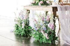 flowers and greenery are arranged on the side of a table