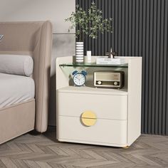 a white nightstand with a clock on it next to a bed and a plant in a vase