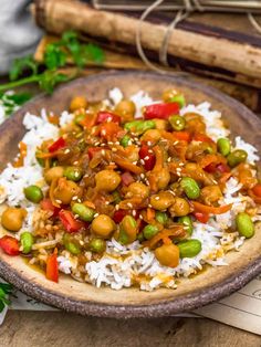 a brown bowl filled with rice and vegetables on top of a wooden table next to some chopsticks