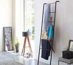 a ladder leaning against the wall with clothes hanging on it and a potted plant next to it