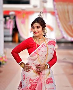 a woman in a red and white sari posing for the camera with her hands on her hips