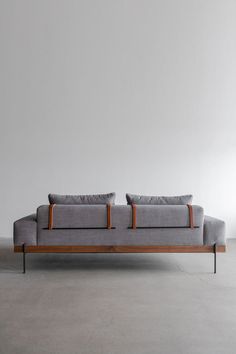 a gray couch with two pillows on it in front of a white wall and floor