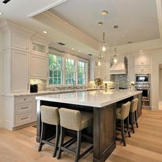 a large kitchen with an island in the middle and four bar stools at the end