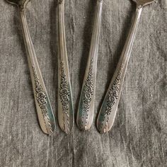 three silver spoons with ornate designs are sitting on a linen covered tablecloth, next to each other