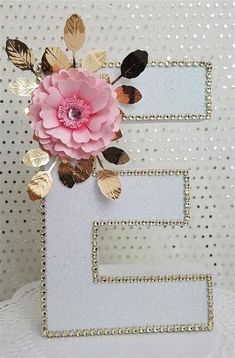 the letter e is decorated with gold leaves and a pink flower on top of it