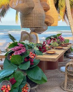 an outdoor dining table set up on the beach with tropical plants and flowers in baskets