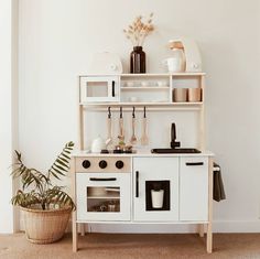 a small white kitchen with an oven and shelves on the wall next to a potted plant