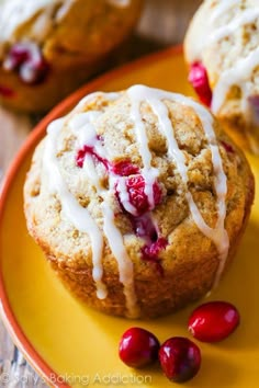 two cranberry muffins with icing on a yellow plate next to some cranberries