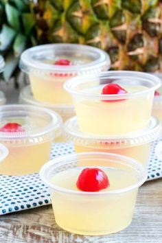 four plastic cups filled with fruit on top of a wooden table next to a pineapple