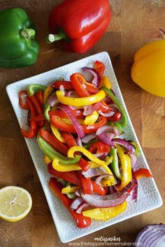 a white plate topped with sliced bell peppers and onions next to lemon wedges on a wooden table