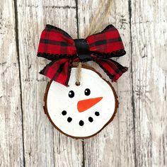 a wooden ornament with a red and black bow hanging on a wood plank