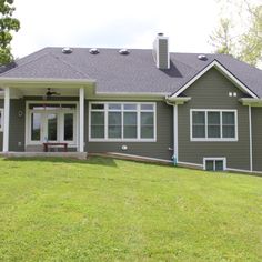 a gray house with white trim on the front and side windows, sitting on a green lawn