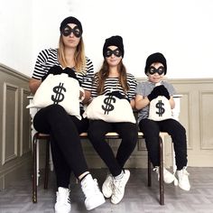 three people sitting on a bench wearing black and white bags with dollar signs painted on them