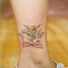 a woman's foot with a book and flowers tattoo on her left side ankle