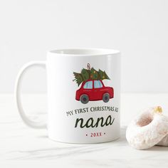 a white coffee mug with a red car and christmas tree on it next to a donut