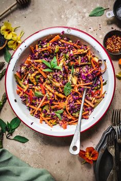 a large bowl filled with colorful salad next to silverware and utensils on a table