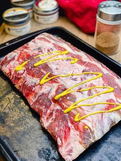 raw meat on a baking sheet with yellow mustard drizzled around the edges