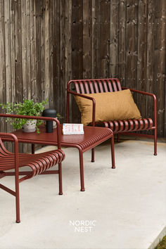 two chairs and a table sitting on a patio next to a wooden fence with plants