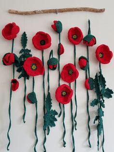 a group of red flowers hanging from a wall next to a stick and twig