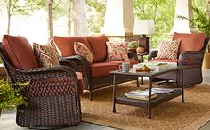 an outdoor living room with wicker furniture and red pillows on the couches,