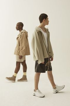 two men walking down the street in shorts and hoodies, one wearing a backpack