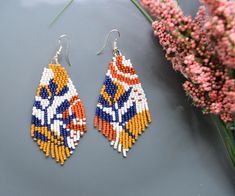 a pair of beaded earrings sitting on top of a table next to pink flowers