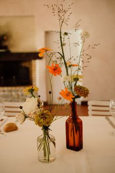 two vases filled with flowers on top of a white table cloth covered dining room table