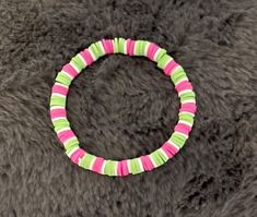 a pink, green and white bracelet on top of a gray fur textured surface