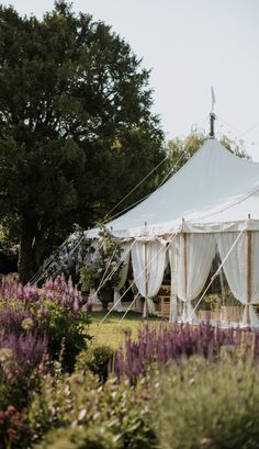 a large white tent sitting in the middle of a lush green field filled with purple flowers